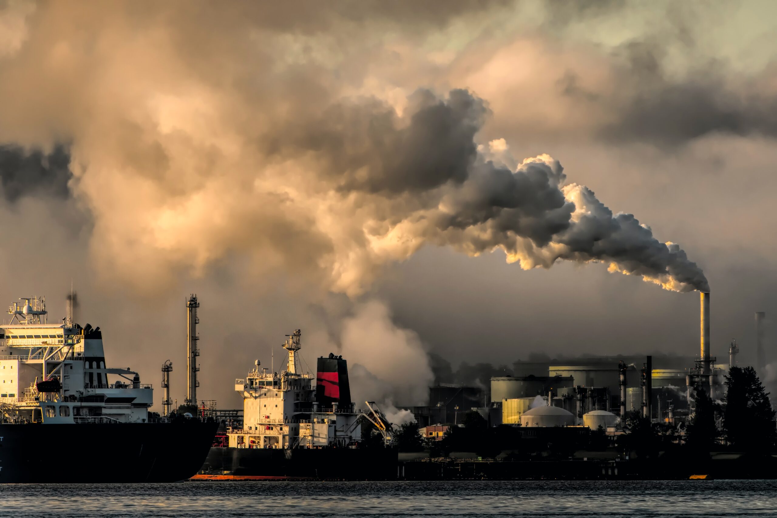 Smoke billowing out of factory smokestacks behind a boat on the water